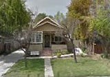 A quaint residential house with a front porch, surrounded by trees and a green lawn.