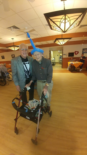 Two friends enjoying a lighthearted moment at an assisted living facility, showcasing creativity with a balloon hat.