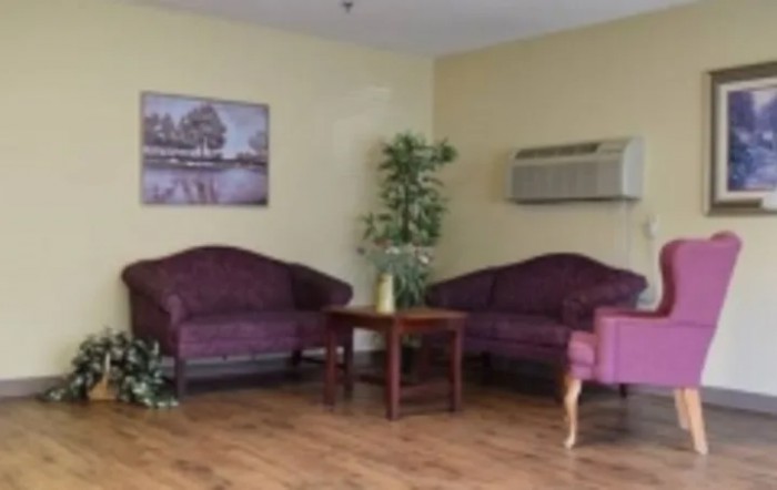 A cozy living room with purple sofas, a wooden table, and an indoor plant beside an air conditioner.