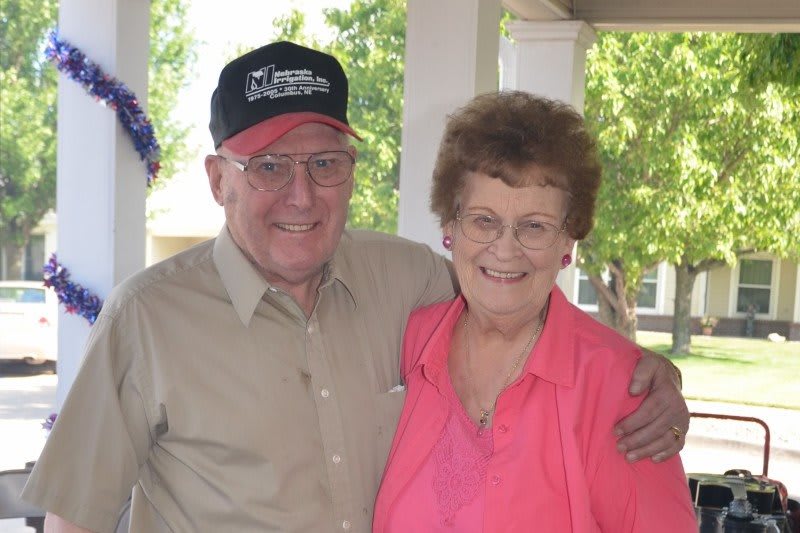 An elderly couple smiling while posing together outdoors.