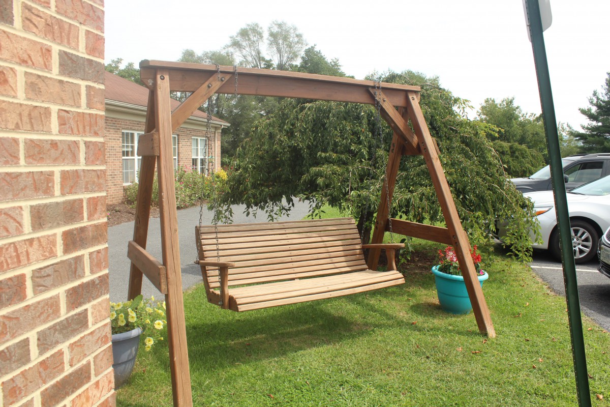 A wooden swing set in a garden area, surrounded by grass and potted plants.
