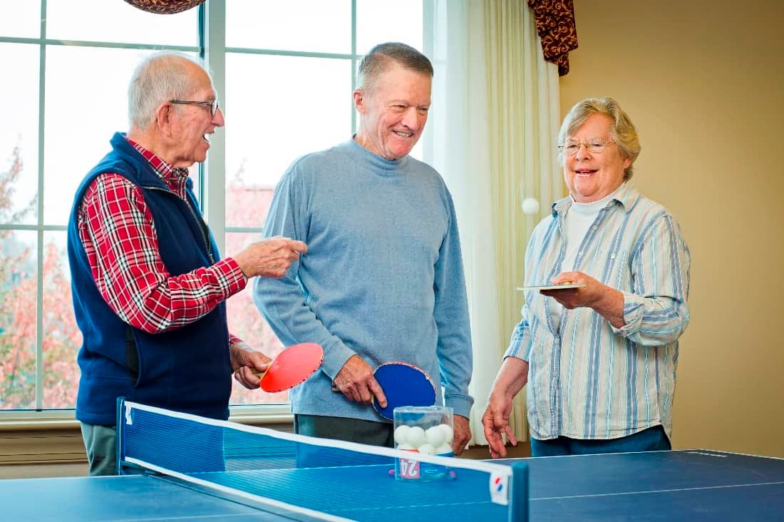A group of seniors enjoying a game of table tennis indoors.