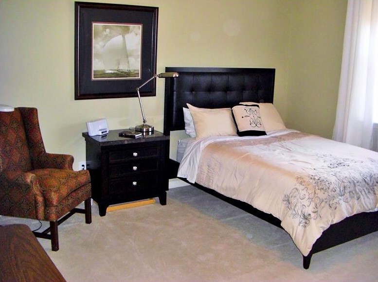 A cozy bedroom with a bed, nightstand, lamp, and chair.