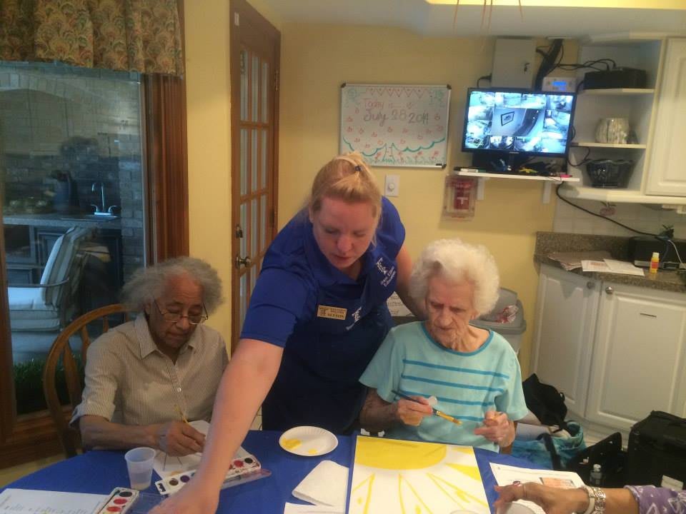 Caregiver assisting elderly individuals with a painting activity at a community center.