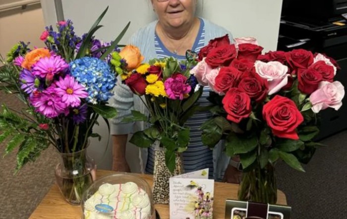 A woman smiles behind a table adorned with vibrant flower bouquets and greeting cards.