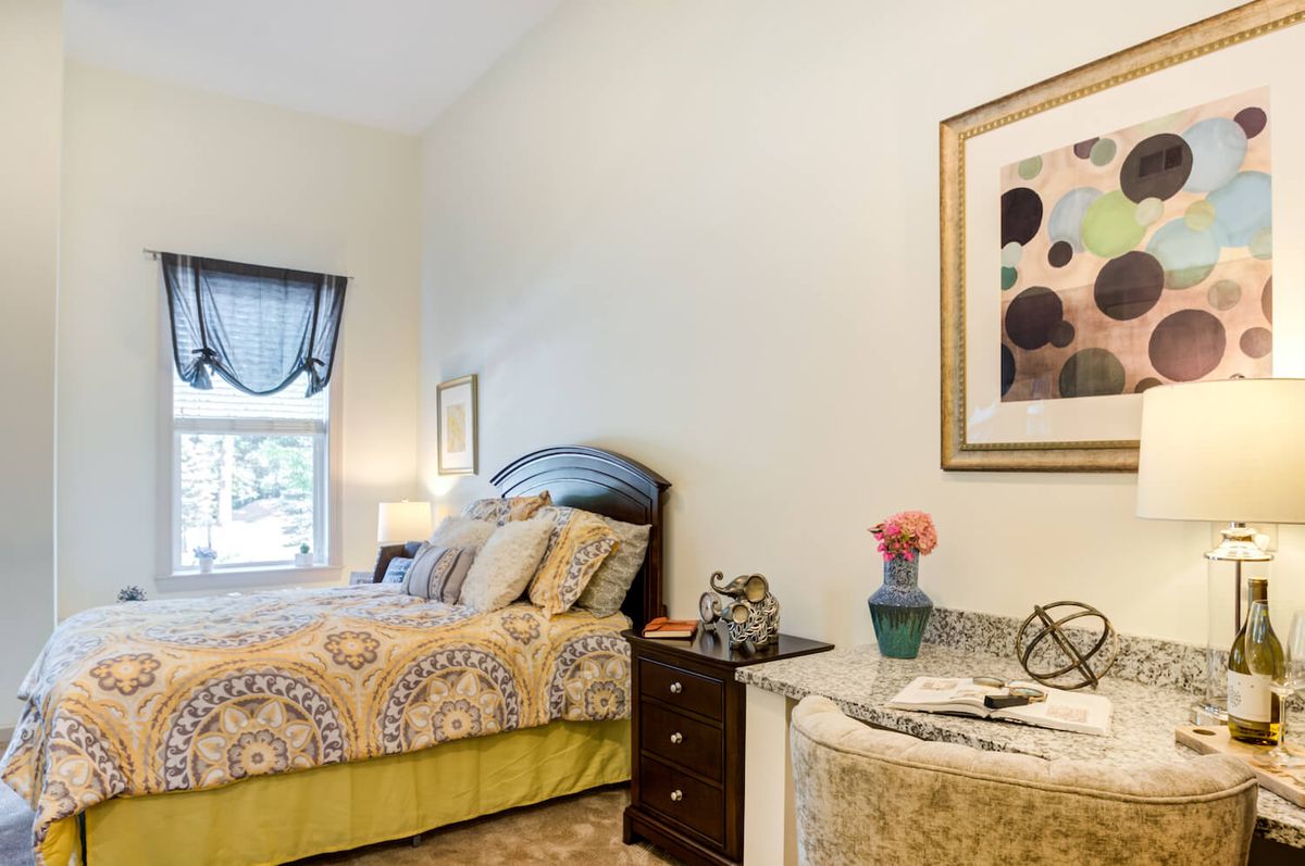 A cozy bedroom with a neatly made bed, nightstand, lamp, and artwork on the wall.
