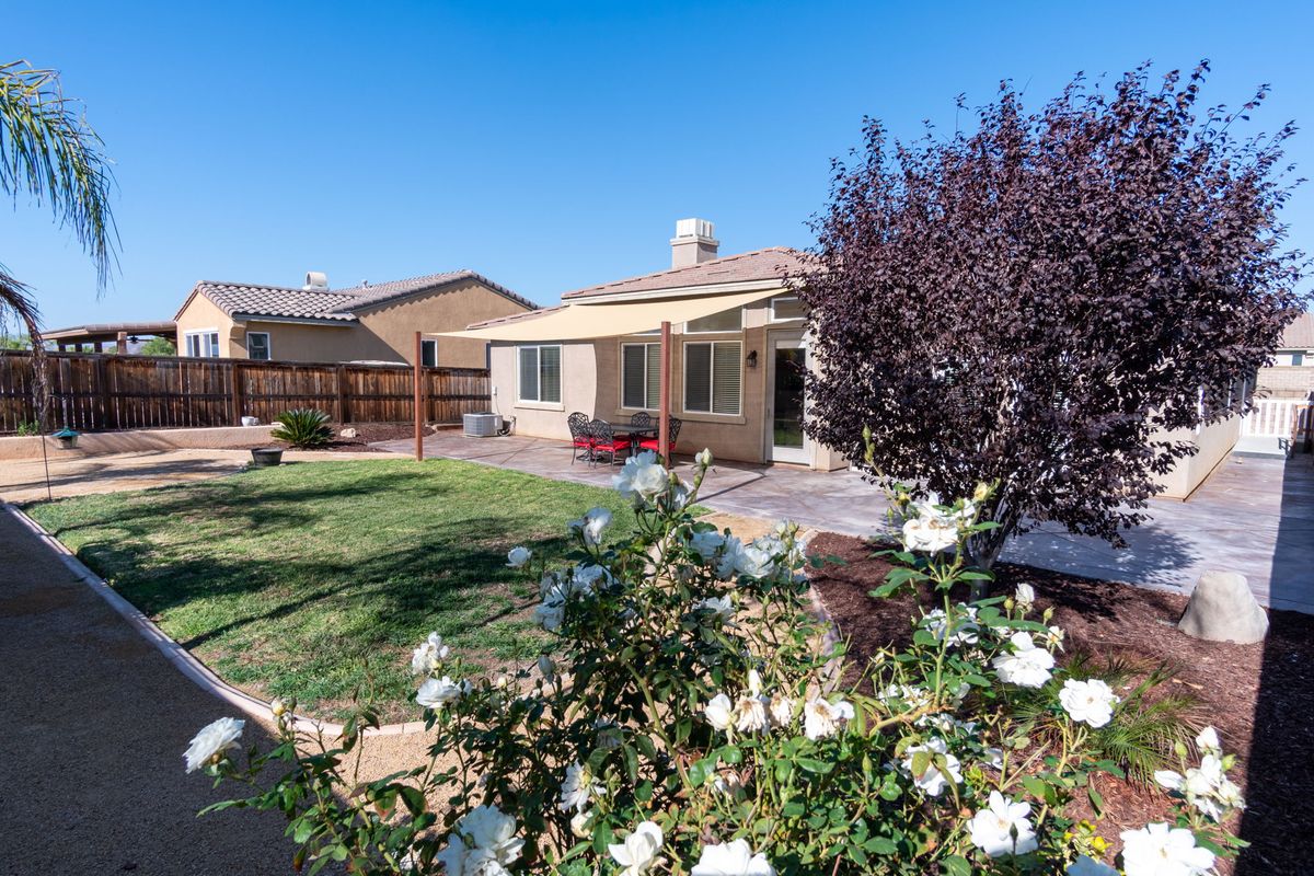 A well-maintained backyard with a lawn, flowers, and trees adjacent to a house.