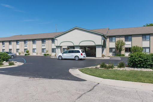 A hotel building with a parking lot and a white vehicle parked in front during the daytime.