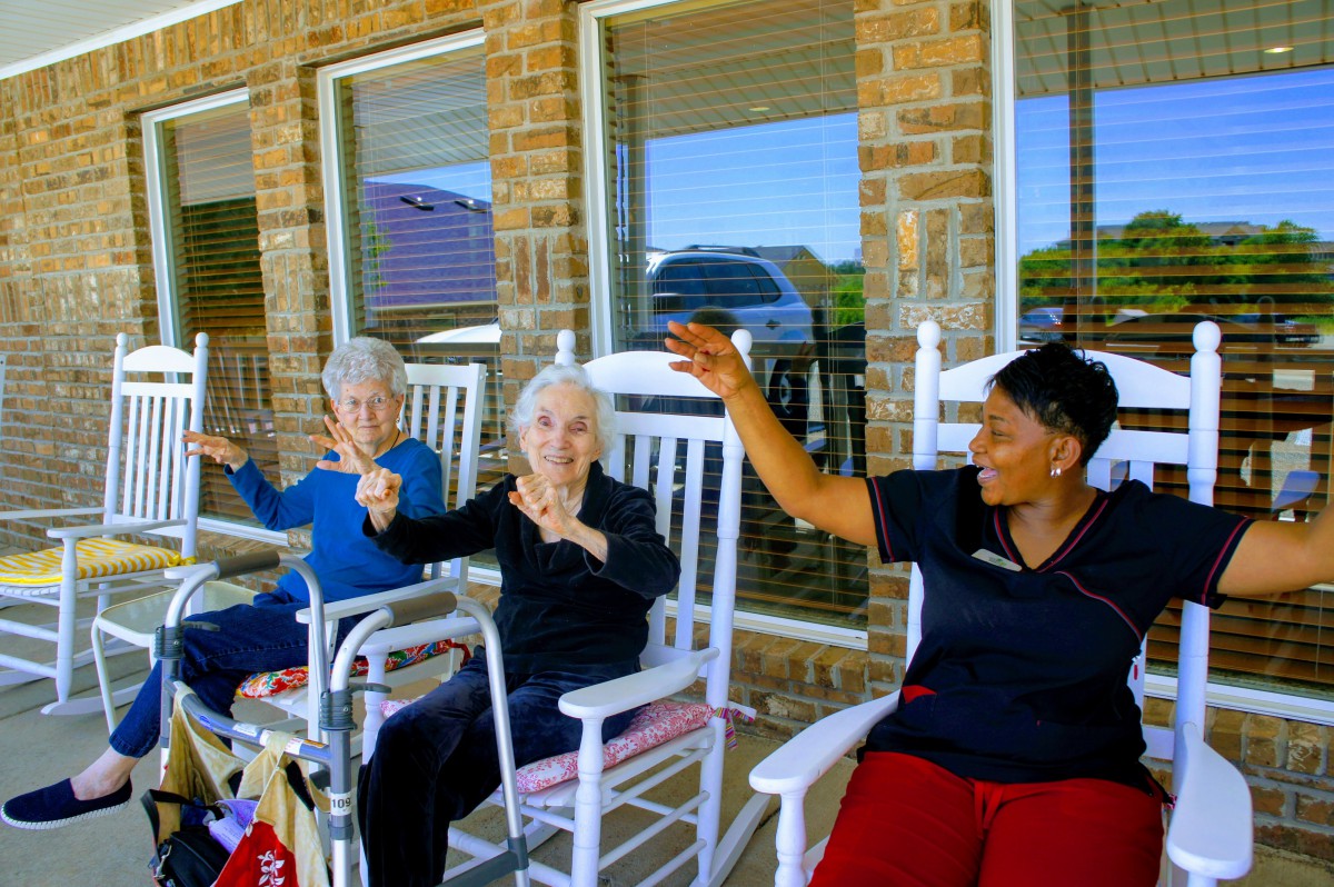 Seniors exercising outdoors with a caregiver in rocking chairs.