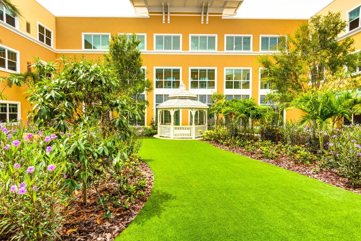 A vibrant garden with a lush green lawn in front of a yellow building.