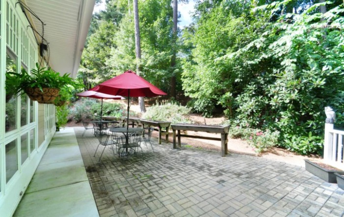 A tranquil patio area with tables and red umbrellas surrounded by lush greenery.