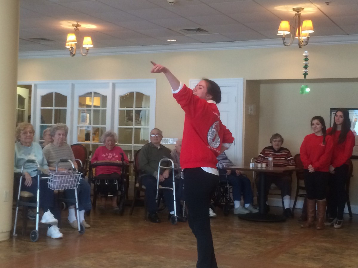 A performer entertains an elderly audience with a dance routine in a community setting.