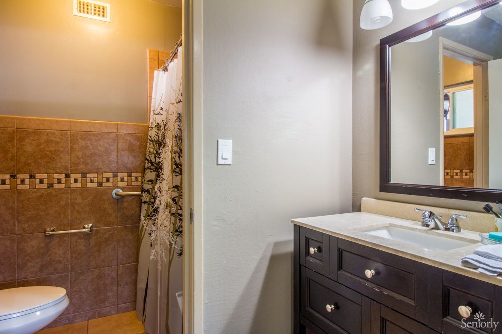 A cozy bathroom with a dark wood vanity, a mirror, and a tiled shower area.