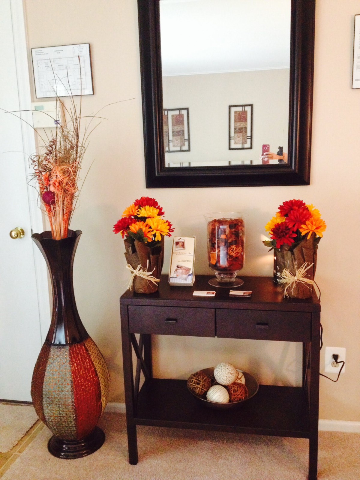 A beautifully decorated entryway table with autumn-themed flowers, a large mirror, and an elegant vase.