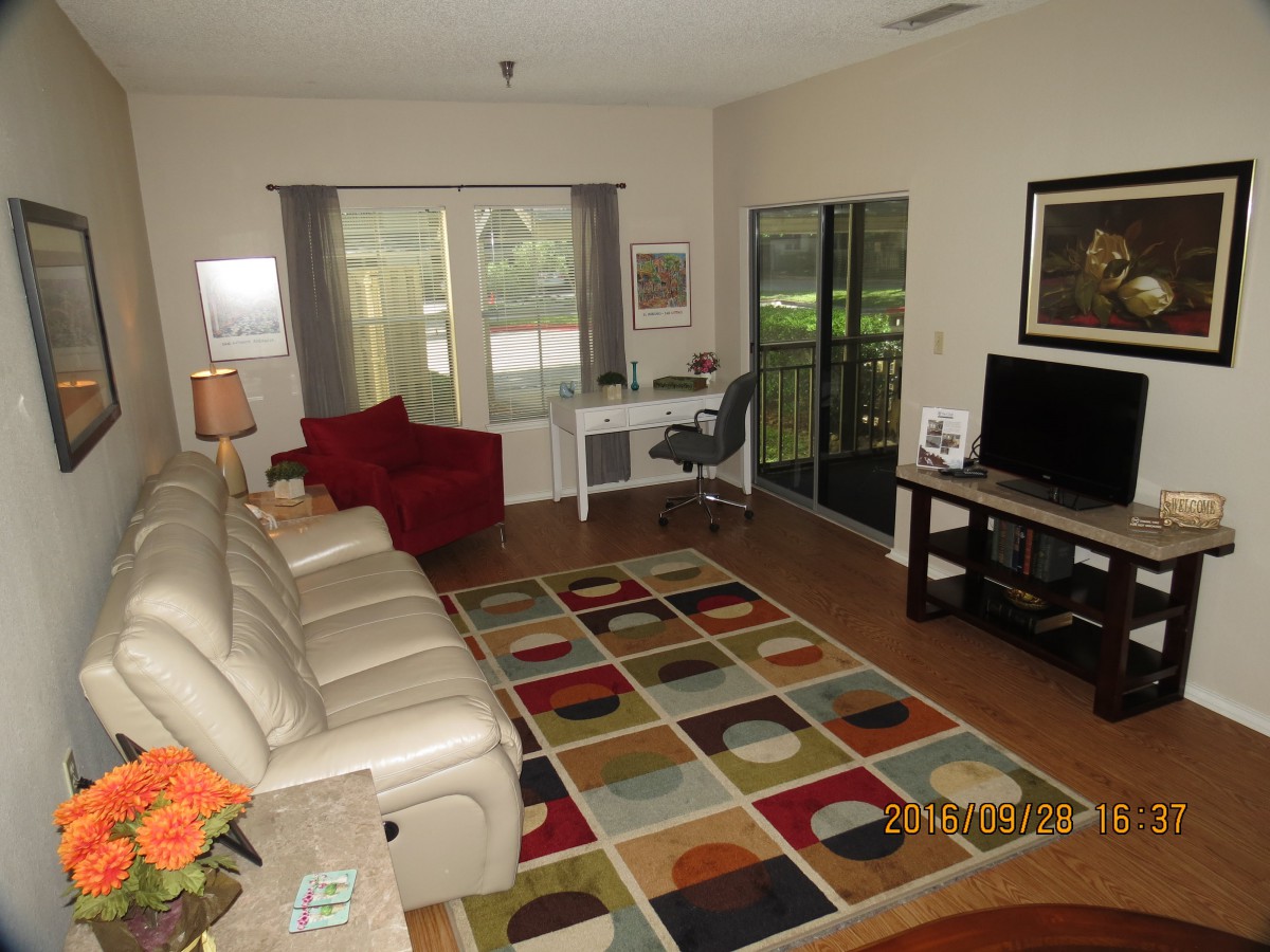 A cozy living room with a colorful rug, leather sofa, and a work desk by the window.