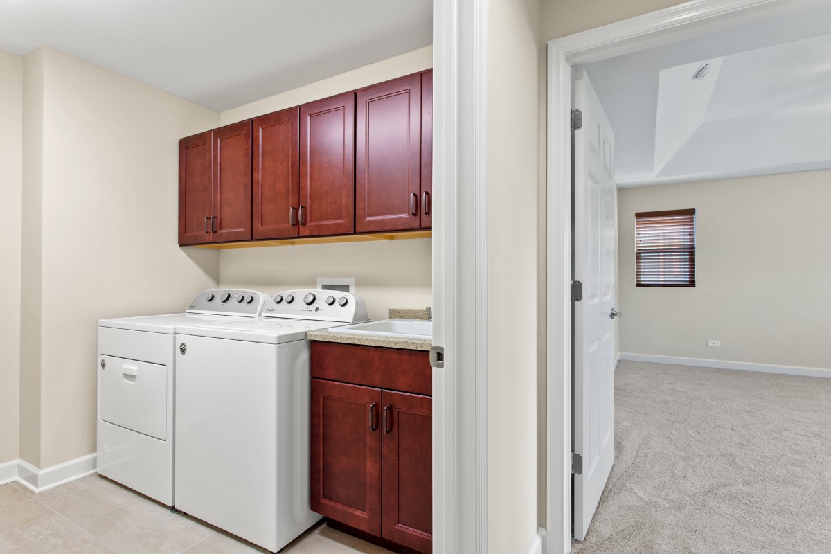 A laundry room with a washer, dryer, and wooden cabinets.