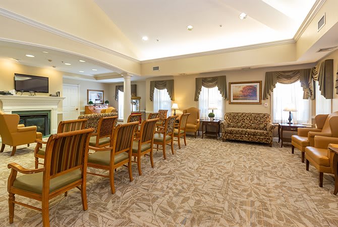 A spacious and well-lit waiting area with rows of chairs and a sofa, decorated with artwork and large windows.