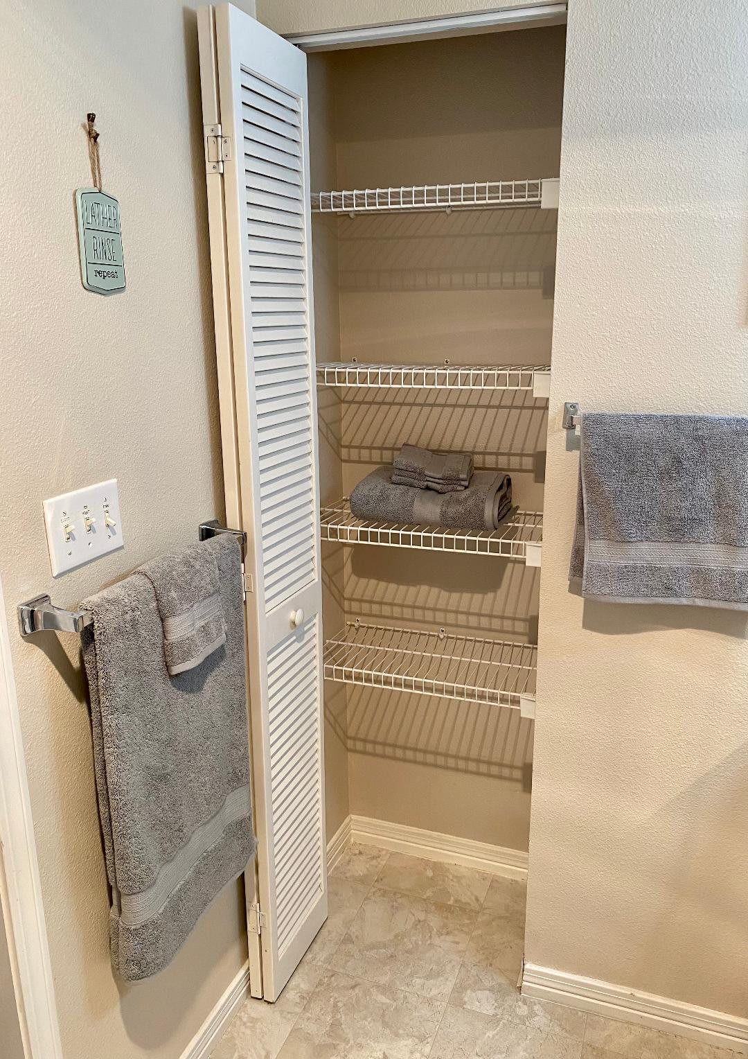 A neatly organized bathroom linen closet with grey towels on wire shelves.