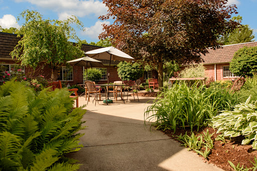 A serene outdoor garden area with patio furniture shaded by an umbrella, surrounded by lush greenery.