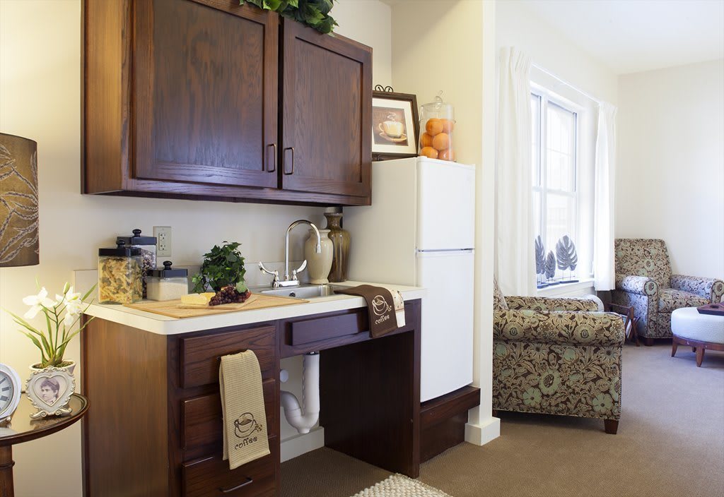 A small kitchen area with dark wood cabinets, a sink, and a white refrigerator, adorned with decorative items and towels.