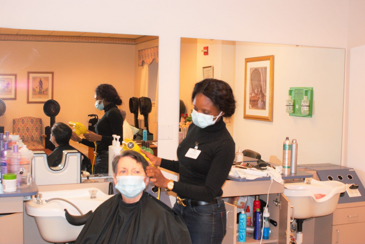 A hairstylist wearing a mask is cutting the hair of a customer, who is also masked, in a salon setting.