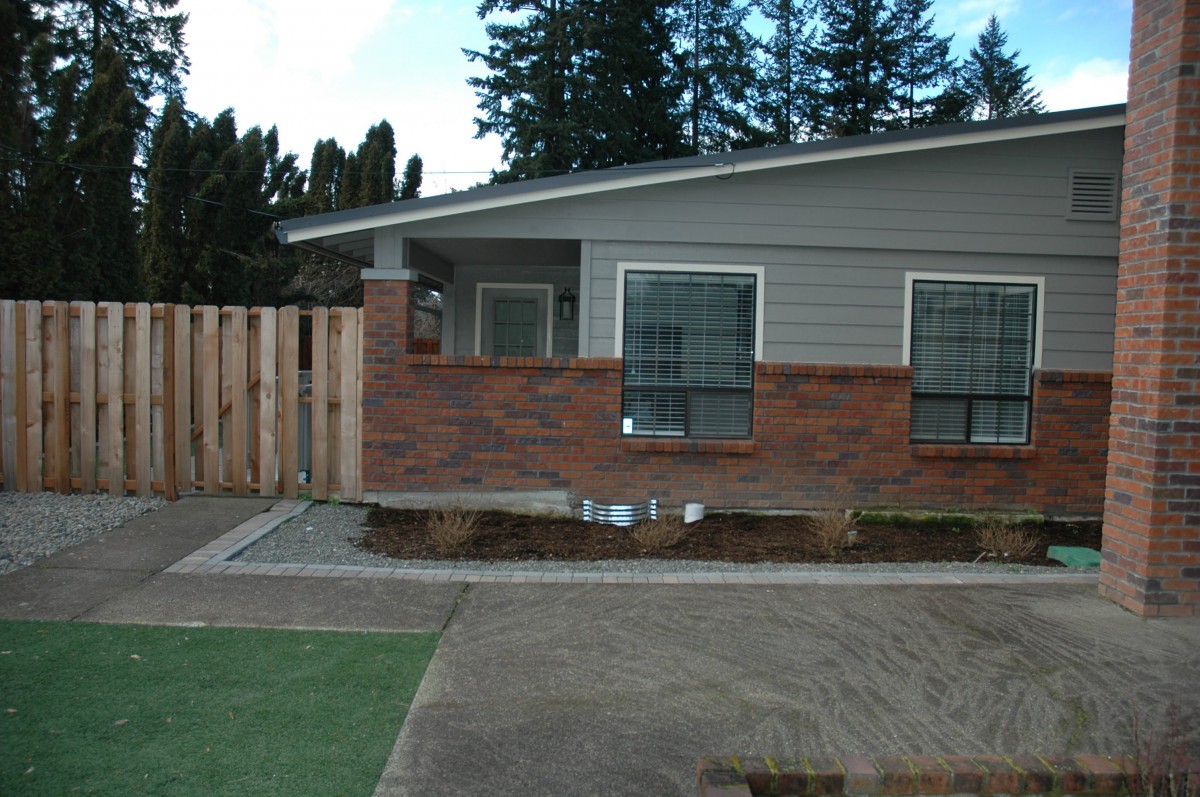 A residential house with brick exterior, a driveway, and a wooden fence surrounded by trees.