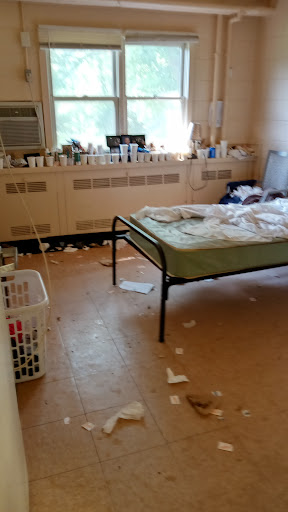 A cluttered bedroom with a mattress, a laundry basket, and scattered papers.