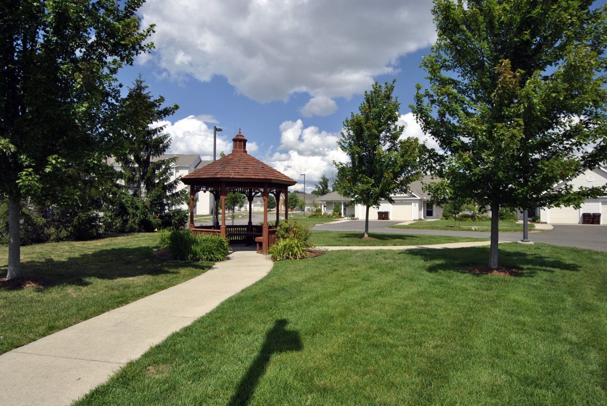 A peaceful park scene with a gazebo, lush green grass, and a clear blue sky dotted with clouds.