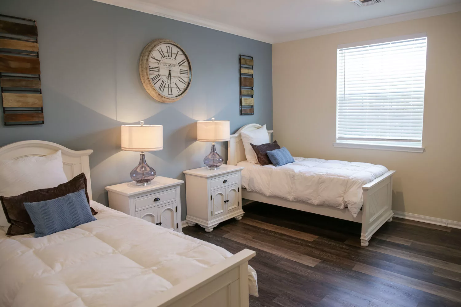 A cozy bedroom with two single beds, decorated with a large wall clock and matching nightstands with lamps.