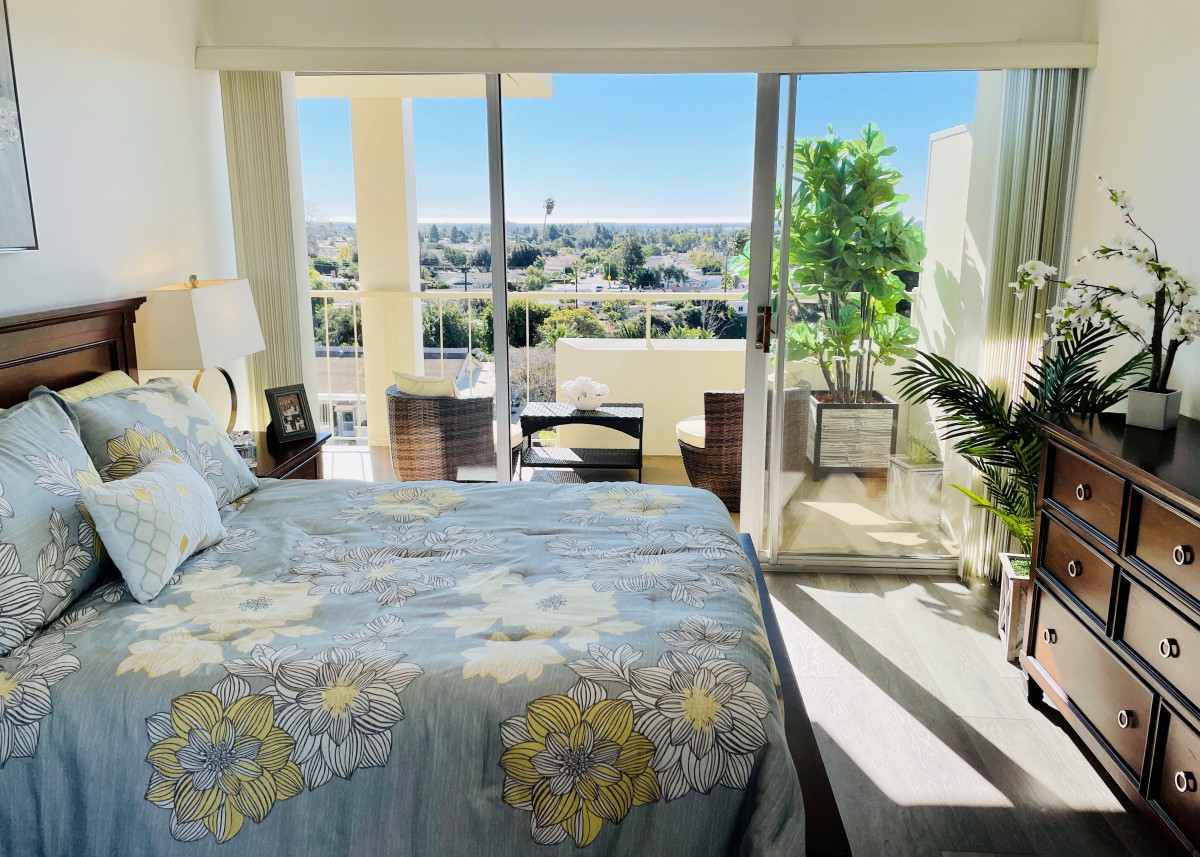 A bright and modern bedroom with a large bed, opening onto a balcony with a scenic view.