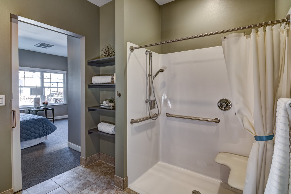 A modern bathroom featuring an accessible shower with grab bars and adjacent shelving stocked with towels.