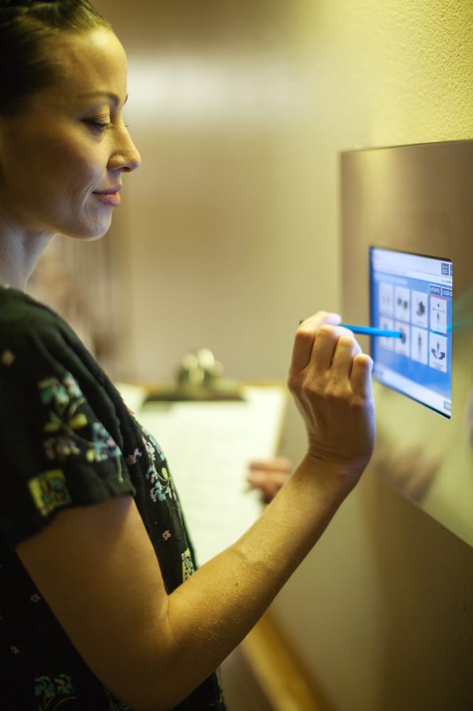 A woman interacts with a touchscreen device indoors.