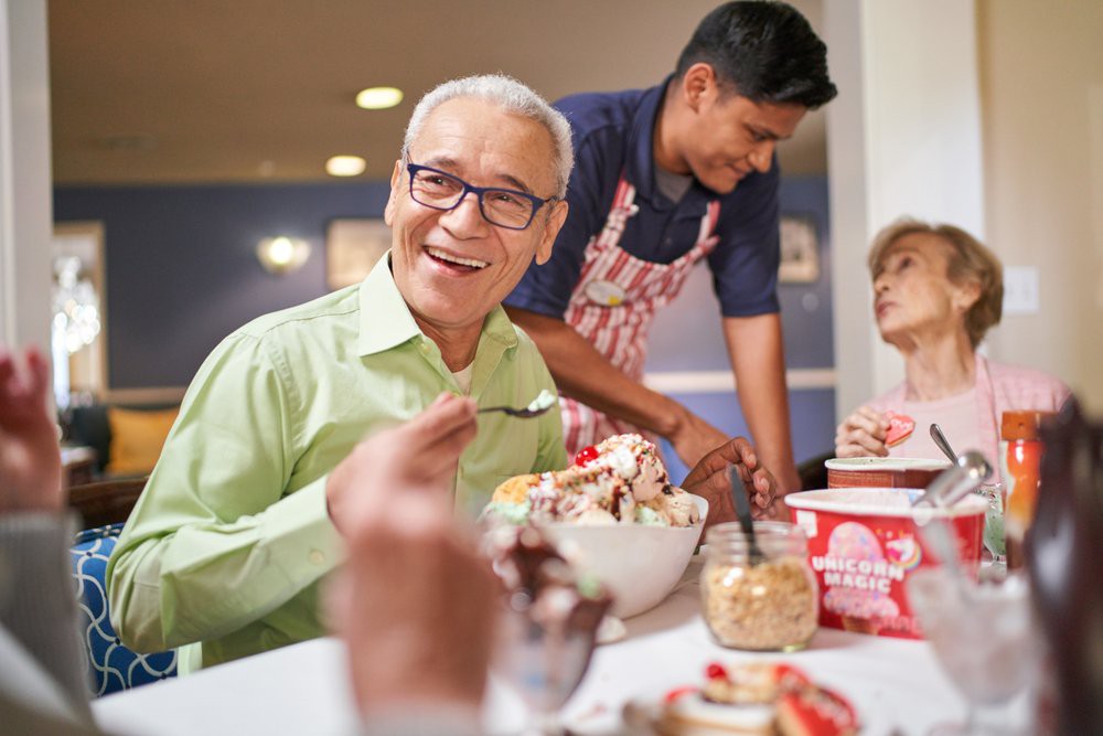A group of people enjoying ice cream at a restaurant, with one man in focus smiling while holding a spoon.