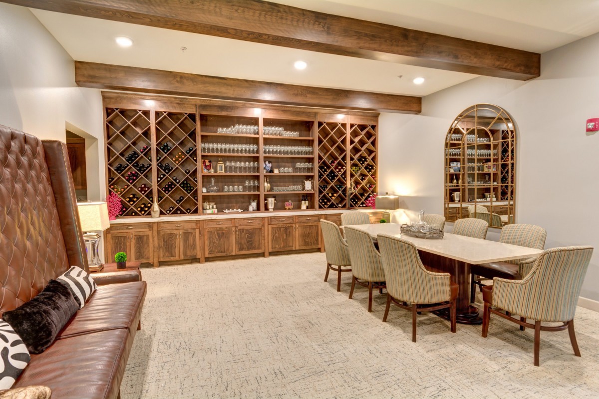 A cozy wine cellar with a dining area featuring shelves filled with bottles, a large table, and comfortable chairs.
