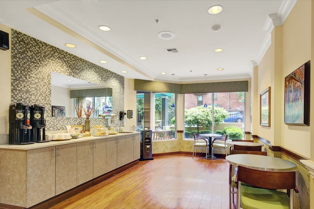 A modern cafe with a minimalist design and wood flooring, featuring a seating area near large windows.