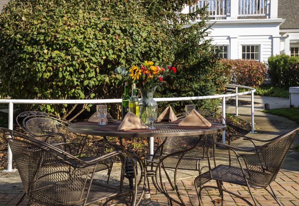 A sunny outdoor patio with a table set for dining, adorned with a vase of colorful flowers.