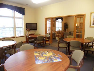 A cozy meeting room with tables, chairs, and a television, featuring a partially completed puzzle on one of the tables.