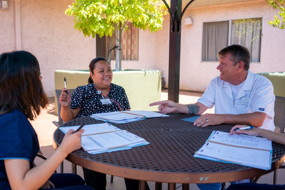 A group of people having a discussion around an outdoor table with documents in hand.