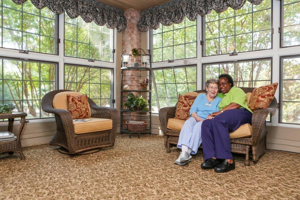 Two women sitting together in a cozy sunroom, surrounded by comfortable seating and large windows.