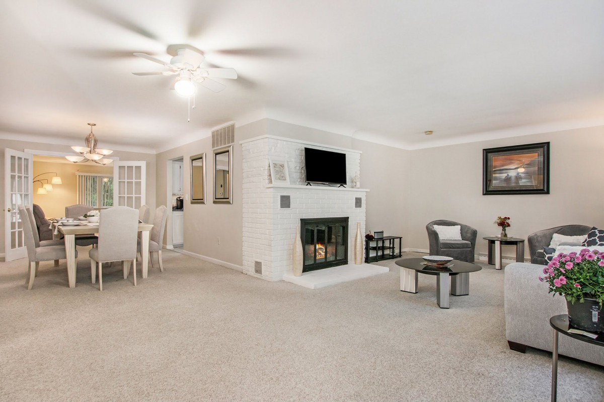 A modern living room with a fireplace and an adjacent dining area, featuring a carpeted floor and contemporary furnishings.