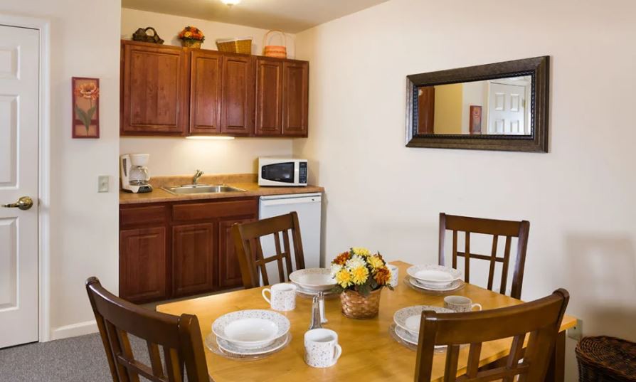 A cozy dining area with a wooden table set for four, adjacent to a kitchen with cabinets and appliances.