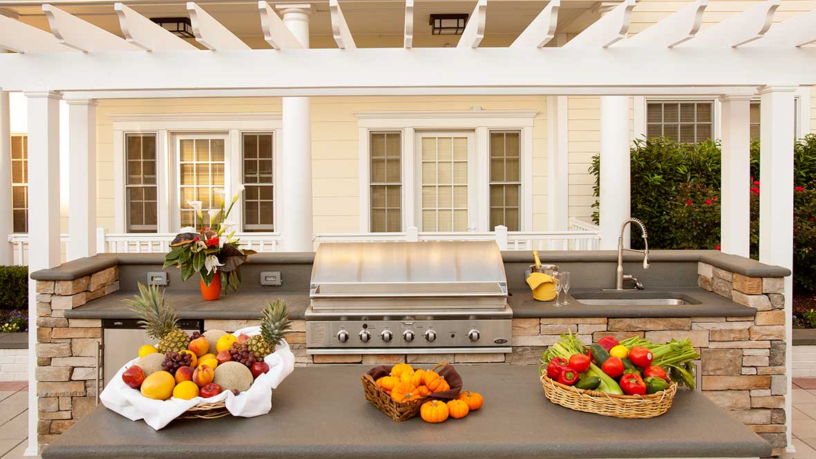 A well-equipped outdoor kitchen featuring a grill and an array of fresh fruits on the countertop.