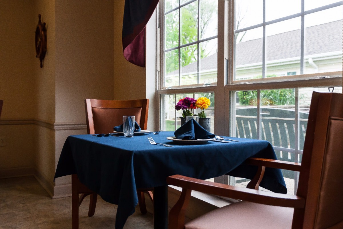 A cozy dining setup by the window, featuring a blue tablecloth and a bouquet of flowers.