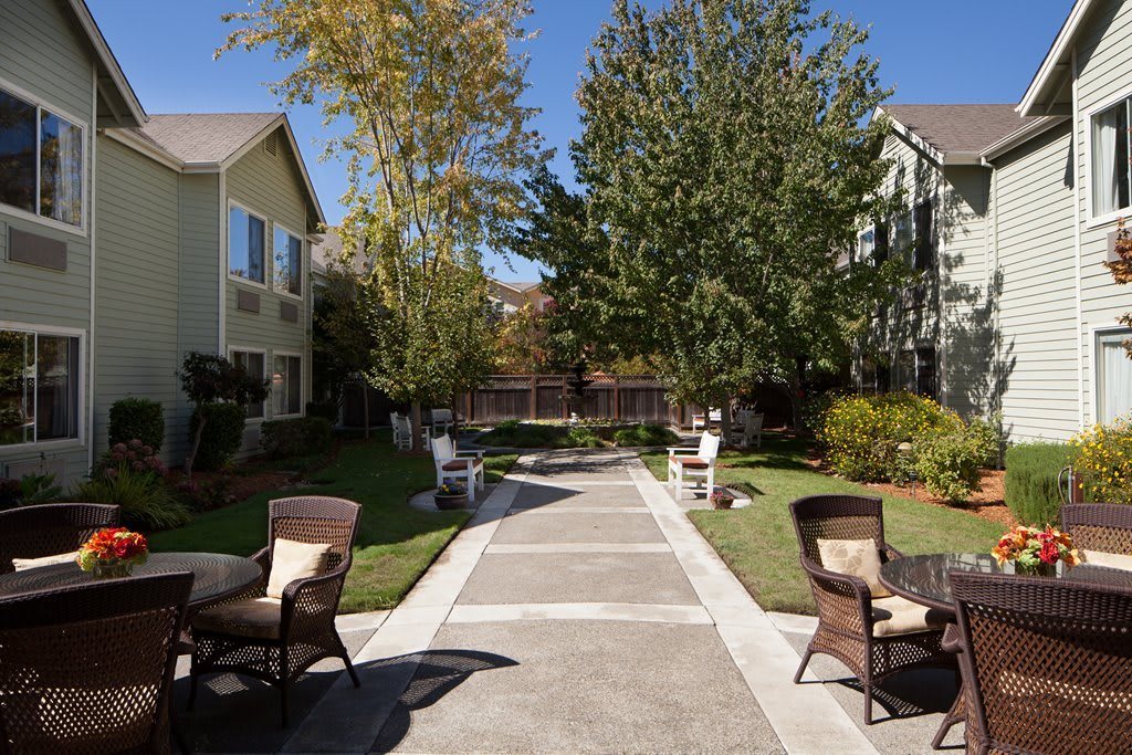 A serene garden pathway lined with tables and chairs between two residential buildings.
