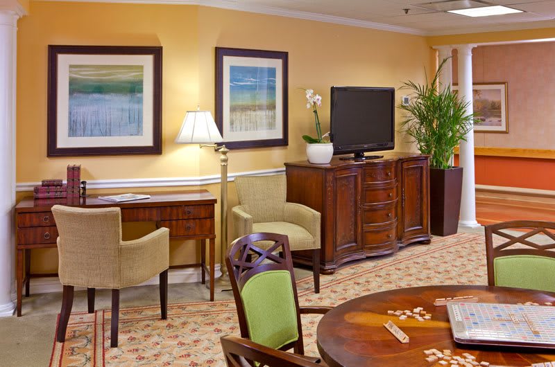 A cozy living room featuring a TV, elegant wooden furniture, and decorative paintings on the wall.