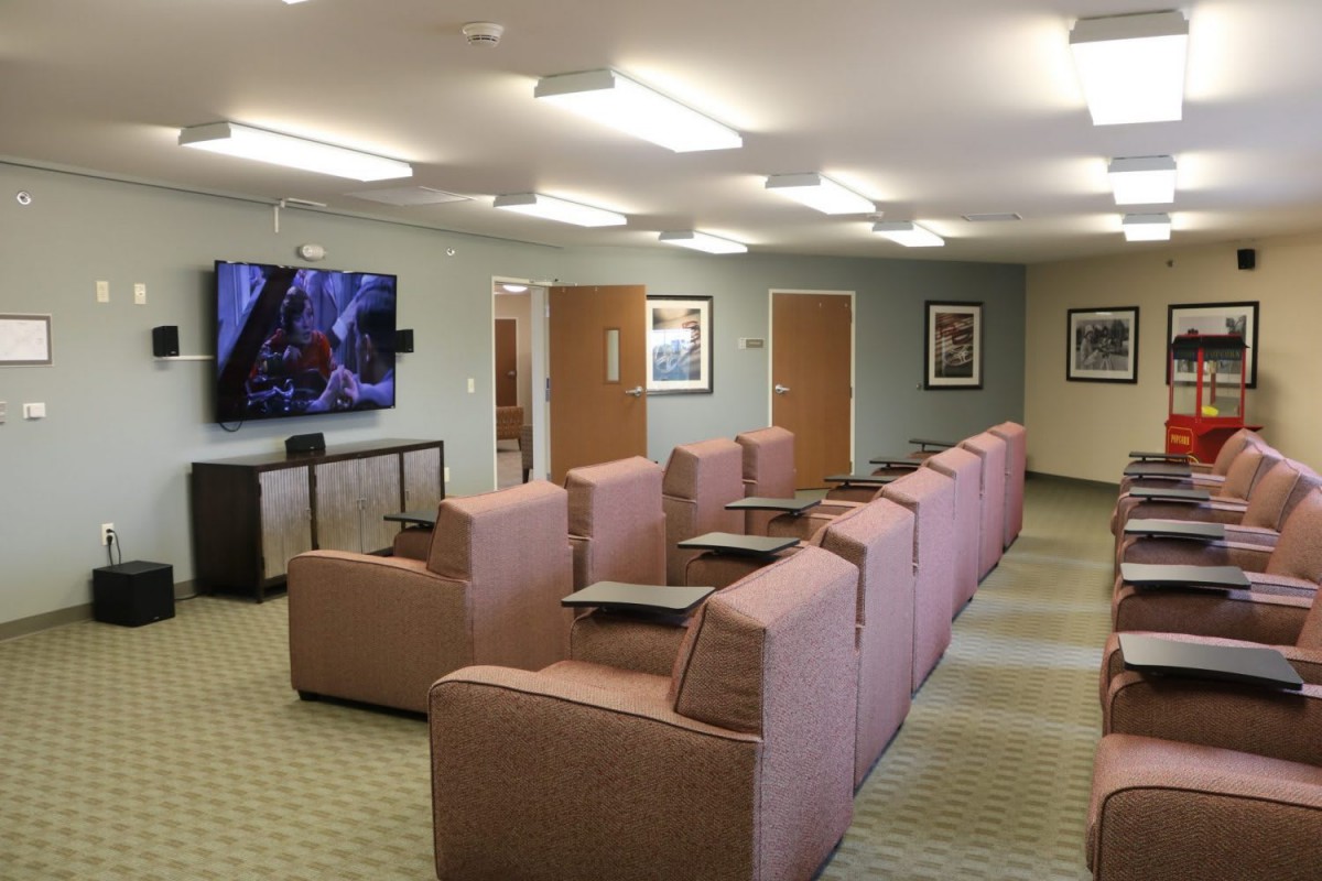A comfortable lounge with rows of cushioned chairs facing a large television, set in a warmly lit interior.
