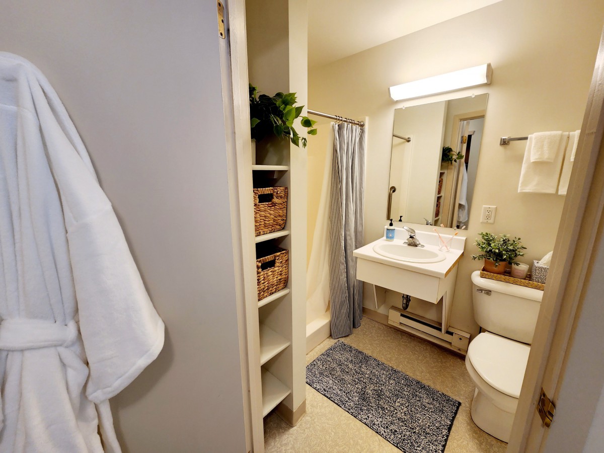 A well-organized bathroom with a sink, toilet, and shower area, complemented by shelves and a bath mat.