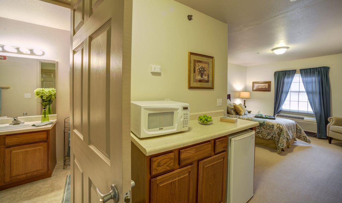 A small kitchenette in a hotel room featuring a microwave, refrigerator, and wooden cabinets.