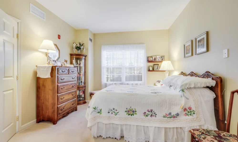 A cozy vintage-style bedroom with a neatly made bed, wooden dresser, and soft lighting from a lamp.