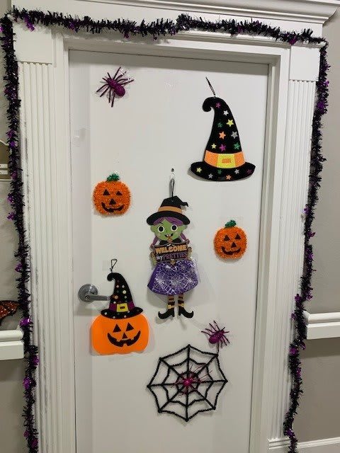 A door decorated for Halloween with witches, pumpkins, hats, and spider webs.